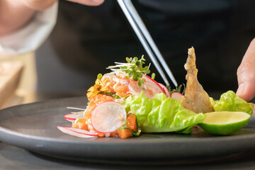 Tweezers chef in Chef's hand decorates Spicy Salmon Salad by micro herb on the food.
