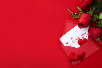 Note that says "I love you" inside an envelope with hearts and roses on red background. Top view. Copy space	