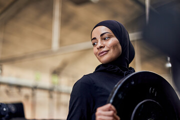 Smiling muslim woman holding a weight in a gym