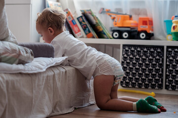 Small child boy toddler hiding in room while pooping in diaper, standing on knees in slight...