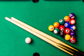 Billiard cues and pyramid of multicolored snooker pool balls on green billiard table.