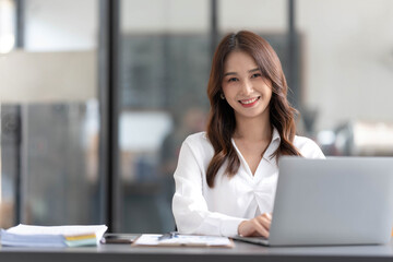 Charming Asian woman working at the office using a laptop Looking at the camera.