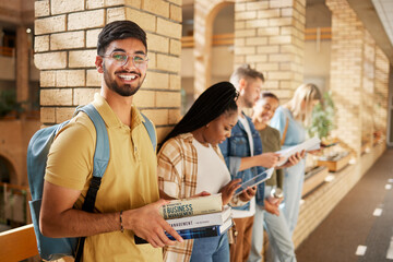 University, hallway and portrait of Indian man and students standing in row together with books at business school. Friends, education and future, happy man in study group on campus in lobby for exam