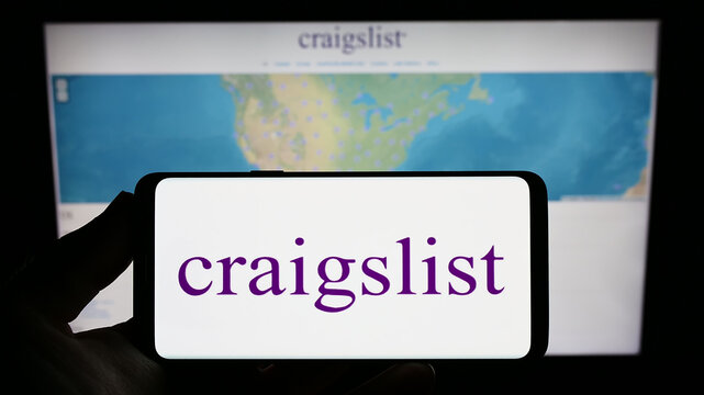 Stuttgart, Germany - 01-08-2023: Person holding smartphone with logo of classified advertisements company Craigslist Inc. on screen in front of website. Focus on phone display.