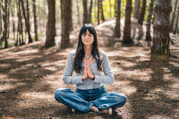 Front view of a woman clasping hands in the woods. Namaste pose.