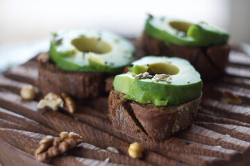 Three avocado sandwiches lie on a wooden board