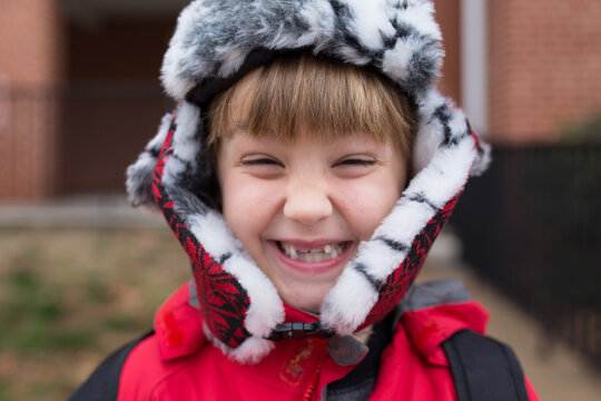 Boy in flap ski hat smiling huge with missing teeth