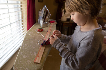 Young boy at ironing board with sewing items around him