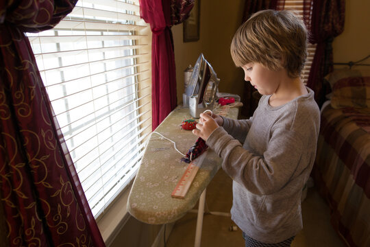 Young boy at ironing board with sewing items around him