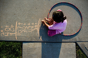 Girl with hula hood on driveway writing chalk numbers