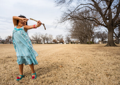 Girl in field pulling back a homemade slingshot