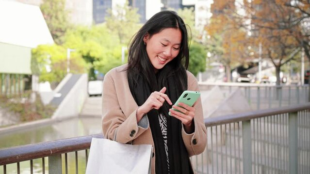 Serious asian business young woman watiching in the cell phone app a message text, outdoors. Unhappy chinese girl reading news on the smartphone. Slow motion. High quality 4k footage