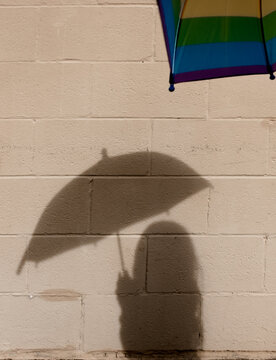 Shadow of colorful umbrella on a concrete block wall