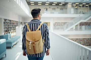 Backpack, library and study with a man student walking in a university bookstore for education or learning. Back, college and research with a male pupil taking a walk in search of reading books - Powered by Adobe