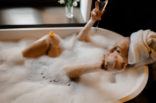 Woman chilling in bubble foam bathtub with champagne 
