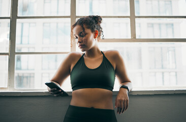 Fototapeta premium Idea, phone and exercise with a sports woman by a window, standing in the gym during a fitnesss workout. Health, thinking and a female athlete using social media or an app to track her training