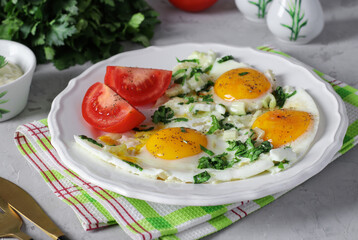 Fried eggs with celery and parsley on a white plate, served with tomatoes, tasty breakfast
