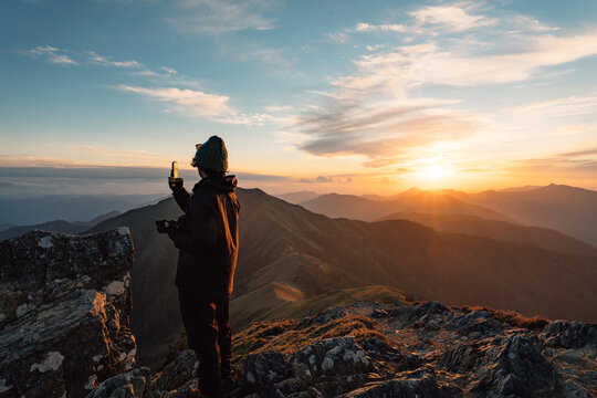 Traveling woman taking photo of sunset in mountains