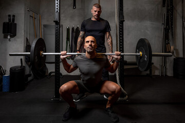 Male athlete with barbell squatting near coach
