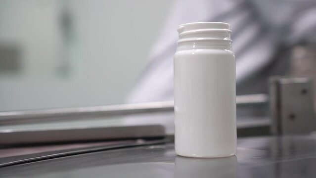 Envasado de medicamentos farmac&eacute;uticos en recipiente de color blanco sobre un cinta giratoria para industria farmac&eacute;utica.