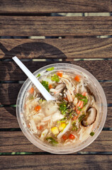 Chicken and mushroom soup in a cheap clear plastic container with a spoon. Affordable lunch in disposable bowl to go