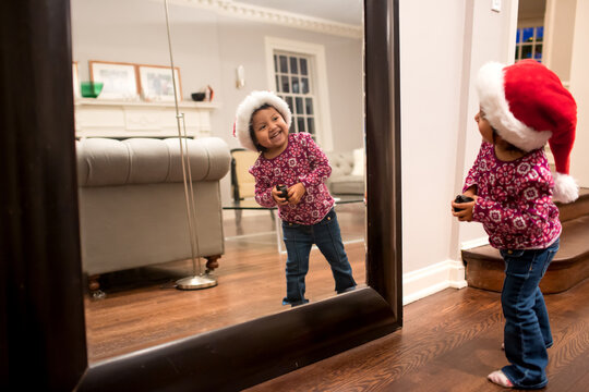 Girl in Santa hat peeking at her reflection in mirror