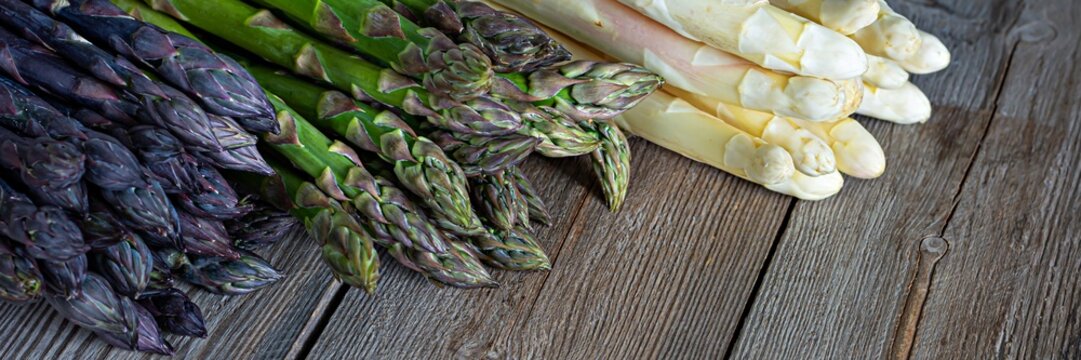 Raw white, purple, green asparagus on wooden background. Healthy food concept, place for copy space. The vegetable is rich in fiber, a natural prebiotic. - Powered by Adobe