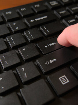 A person's finger pressing the Enter key on a black computer keyboard. Close up, macro shot