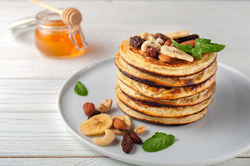 Fresh, delicious pancakes with dried bananas, oranges, nuts and honey on a plate.