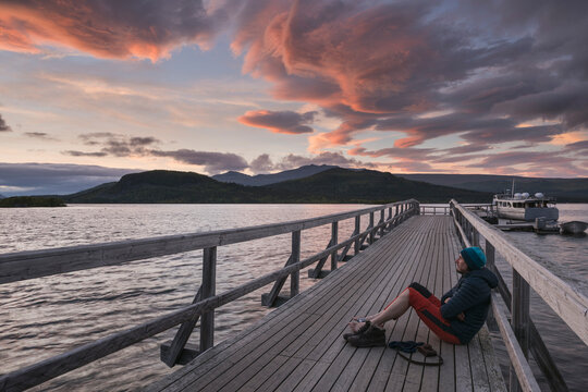 Hiker watches sunset from pier on lake at STF Saltoluokta Fj&Atilde;&curren;llstation, Kungsleden trail, Lapland, Sweden