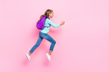 Full size profile portrait of beautiful little girl jumping hurry run use telephone isolated on pink color background