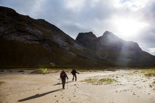 Backpackers hike into the sun above Horseid Beach, Moskenesoya, Lofoten Islands, Norway.