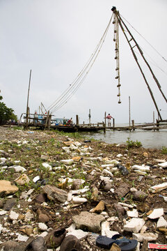 Garbage strewn waterfront with fishing nets in background.