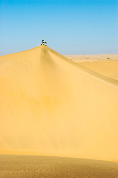 A man sits atop a dun in the Namib Desert, Namibia.