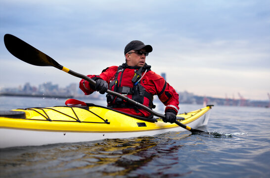 A senior male in his yellow kayak rows in front of the city skyline.