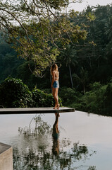 Young travelling girl walking on the edge of an infinity pool in a luxurious home in Ubud, Bali, Indonesia. 