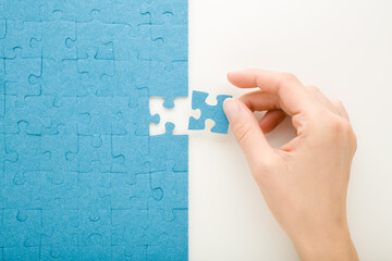 Young adult woman hand holding and putting last one blue puzzle piece on white table background....