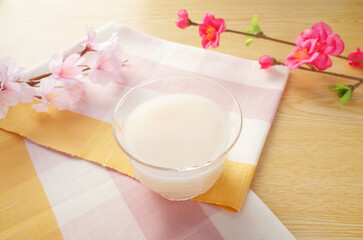 グラスに注がれた甘酒のシーン　桜と梅の花とピンクのチェックの伊勢木綿