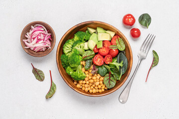 Healthy food in wooden bowl. Chickpeas, lettuce, cherry tomatoes, avocado, broccoli salad. Vegan Budha bowl on light background, top view