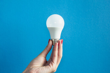 lamp in a woman's hand. female fingers holding LED lamp. idea. New idea or inspiration concept. Concept of startup. blue background. Horizontal image.