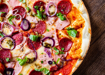 Pizza with Mozzarella cheese, ham, tomato sauce, salami, onion, pepper, Spices and Fresh basil. Italian pizza on wooden table background