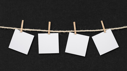 Four blank post it reminders and clothespins attached to a rope on retro black paper background.