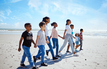 Summer, children and friends walking on the beach, holding hands together for holiday or vacation. Nature, diversity and walk with a kids group bonding by the sea or ocean in the day for community