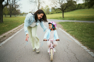 Children, bike and a mother teaching her girl how to cycle in a park while bonding together as a...