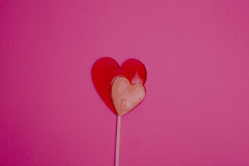 The lollipop is in the shape of two hearts - red and white against the background of the color of the viva magenta. Holiday. Valentine's Day. March 8. Postcard for the holiday.