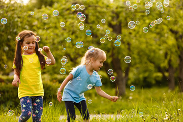 Two cheerful cute girls are playing outdoors with huge soap bubbles