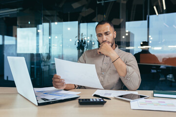 Pensive serious businessman reading financial report, hispanic businessman holding document in...