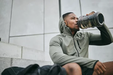 Tuinposter Fitness, relax or black man drinking water in training or exercise for body recovery or workout in Chicago, USA. Hydration, thirsty or tired healthy sports athlete drinks natural liquid in bottle © Siphosethu/peopleimages.com