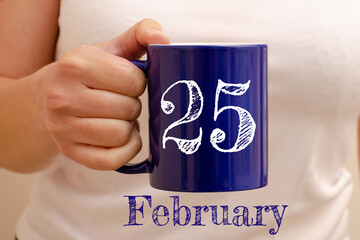 The inscription on the blue cup 25 february. Cup in female hand, business concept