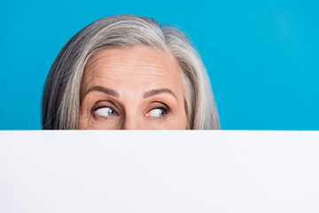 Photo of aged lady empty space wall cover half face look interested proposition isolated on blue color background